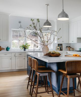 White kitchen with navy island, white countertop, wood and leather bar stools, chrome pendant lights,