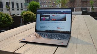 En Lenovo ThinkPad X1 Carbon Gen 9 står öppnad på ett träfärgat bord utomhus.