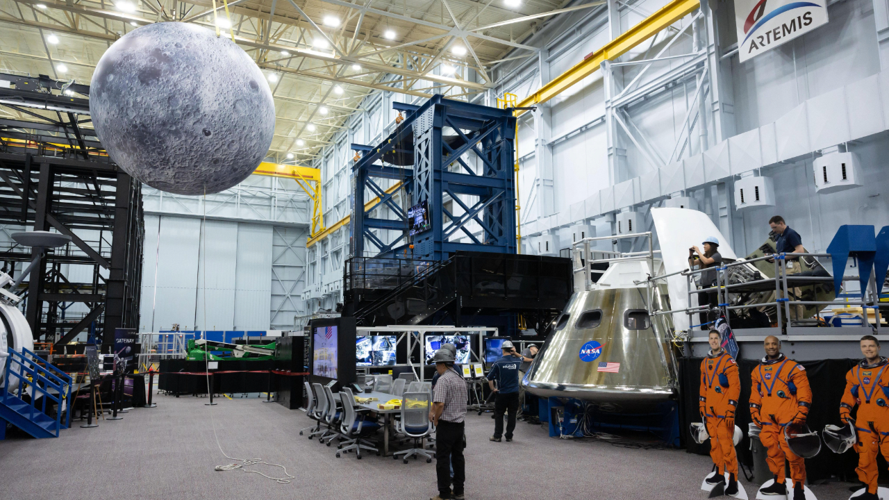 A large inflatable moon hangs over a couple of men below next to cutouts of three astronauts wearing orange jumpsuits
