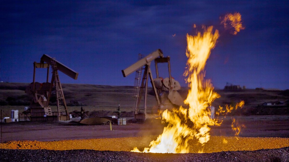 A fire burns in a pit near a natural gas well as methane (CH4) escapes into the atmosphere.