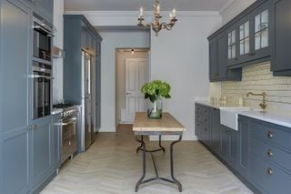 A traditional dark blue galley kitchen with a narrow vintage table island in the middle