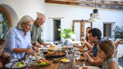 Three generations of Spanish family members seated at dining table for traditional midday meal. Grandparents are serving the food.