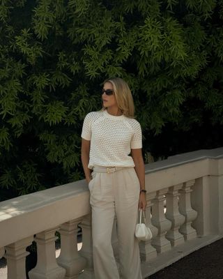 The influencer wears a white handbag with light brown pants and a white short-sleeved crochet sweater.