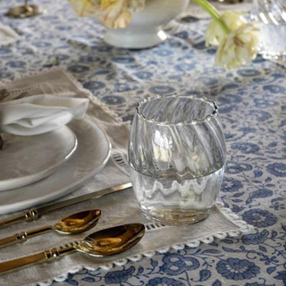 A glass on a table that's been set with a blue patterned tablecloth.