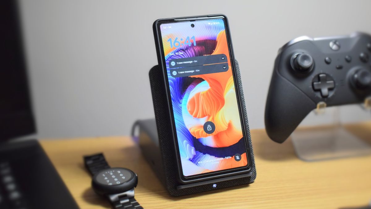 Photo of the Dell Dual Charge Dock with QI wireless charging docking station, showing a Google Pixel 7a in the wireless charging cradle. A Pixel Watch and Xbox Elite Wireless Controller Series 2 are next to the dock.