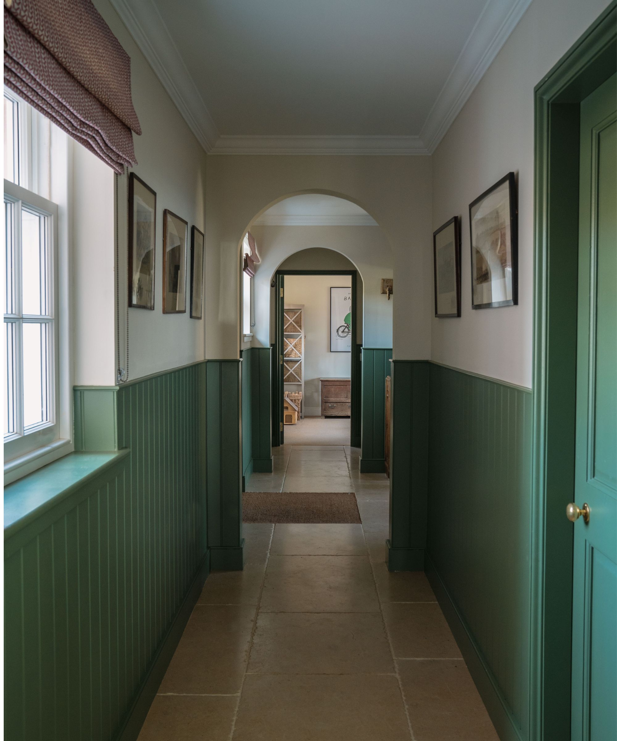 Hallway with Calke Green by Farrow &amp;amp; Ball painted dado rail and doors, arched doorways, slate tiled floor and art on the walls