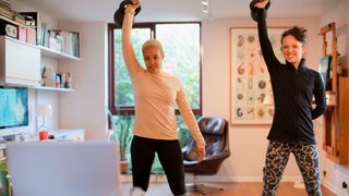 Two women perform the kettlebell press at home