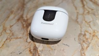 Tronsmart Onyx Ace Pro wireless earbuds inside case with lid closed, lying on a marble table
