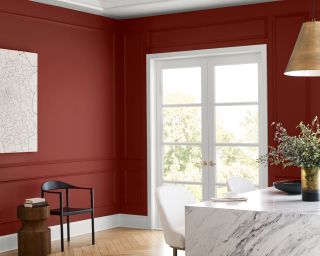 A kitchen with red walls, white trim, and a marble island