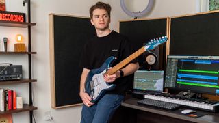 Nick Broomhall sits on his production desk holding his blue Kiesel guitar