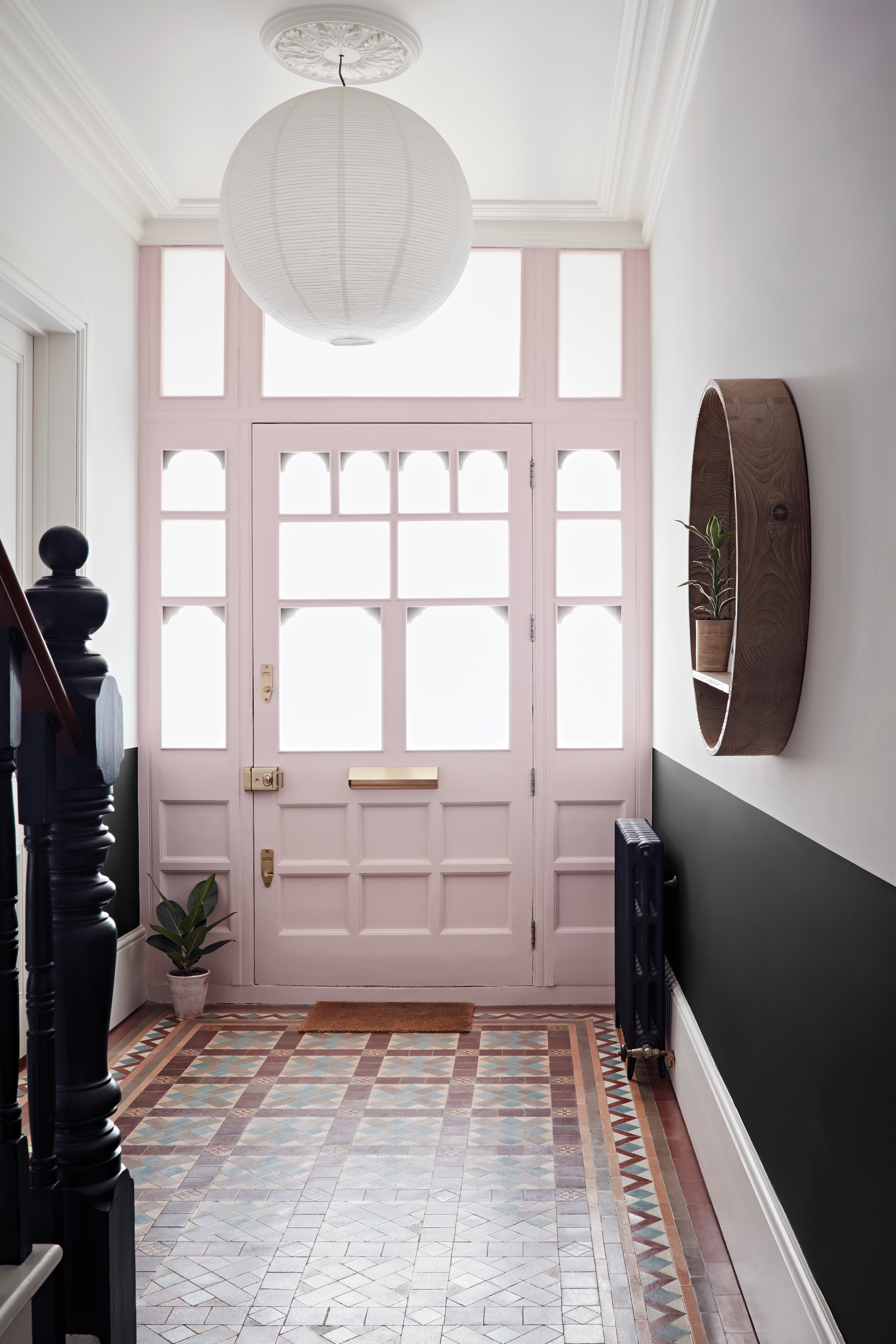 Couloir avec sol carrelé, mur inférieur en noir et supérieur en blanc, et porte d'entrée peinte en rose pâle