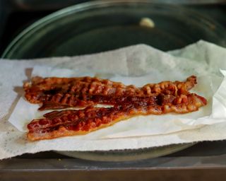 Microwaved rashers of streaky bacon slices on paper towel on glass turntable