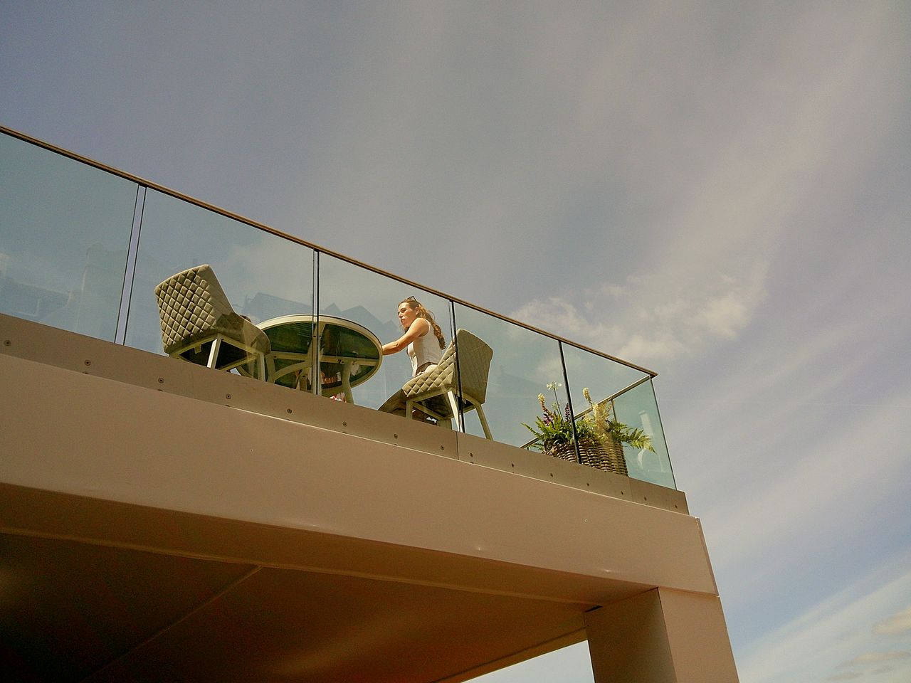 Sample image taken with Camp Snap 2 digital compact camera, showing upward view of woman sitting at table on terrace against blue sky