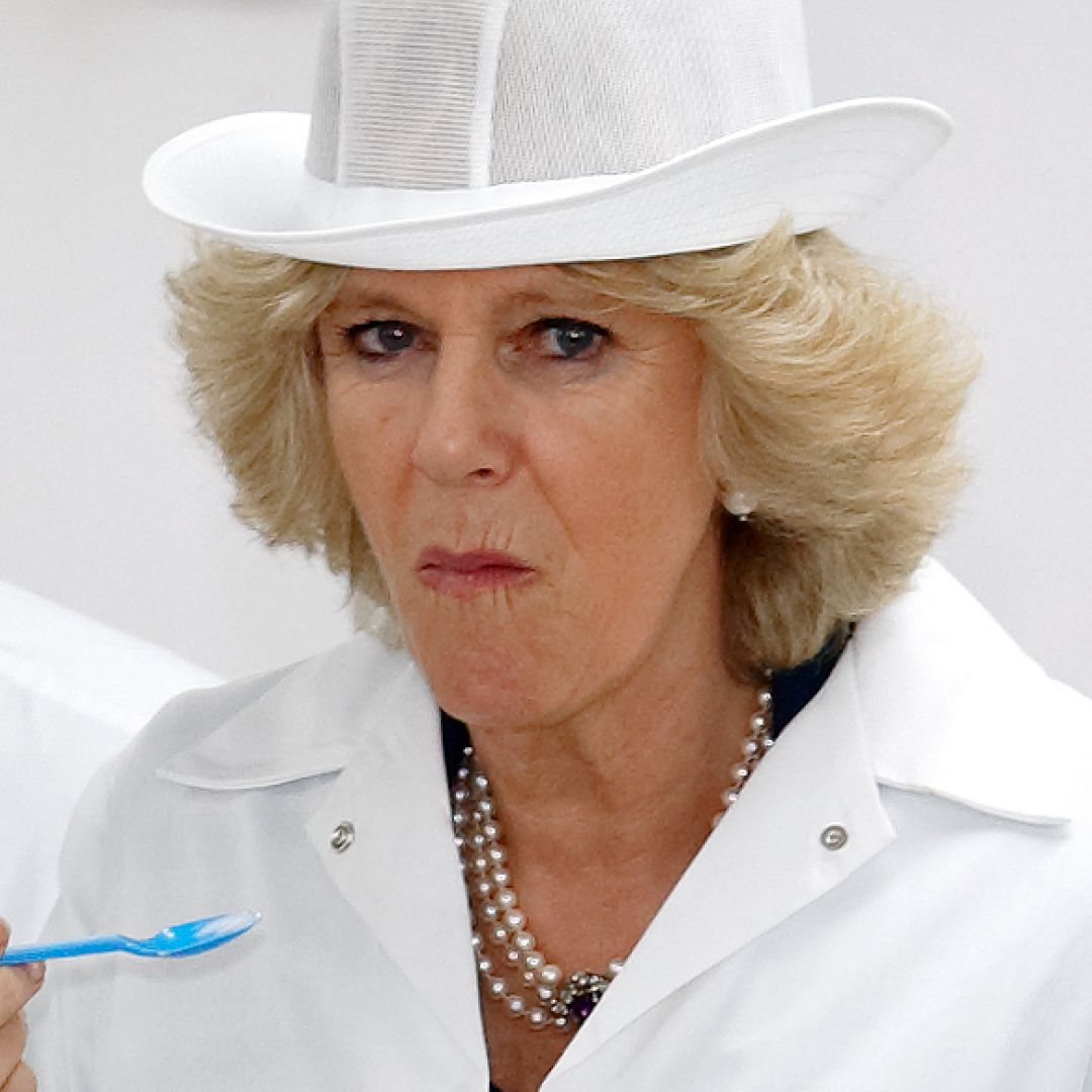 Queen Camilla wears a white coat and hat and eats something