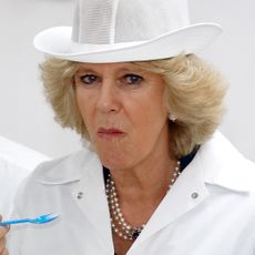 Queen Camilla wears a white coat and hat and eats something