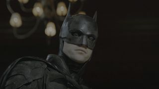 Robert Pattinson's Batman looking down at crime scene as camera flash goes off in The Batman