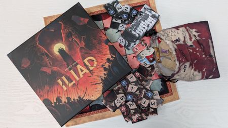 Iliad box, tiles, bag, and board on a white wooden surface