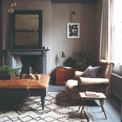 A grey-painted living room with charcoal features, a brown leather armchair and a coordinating ottoman