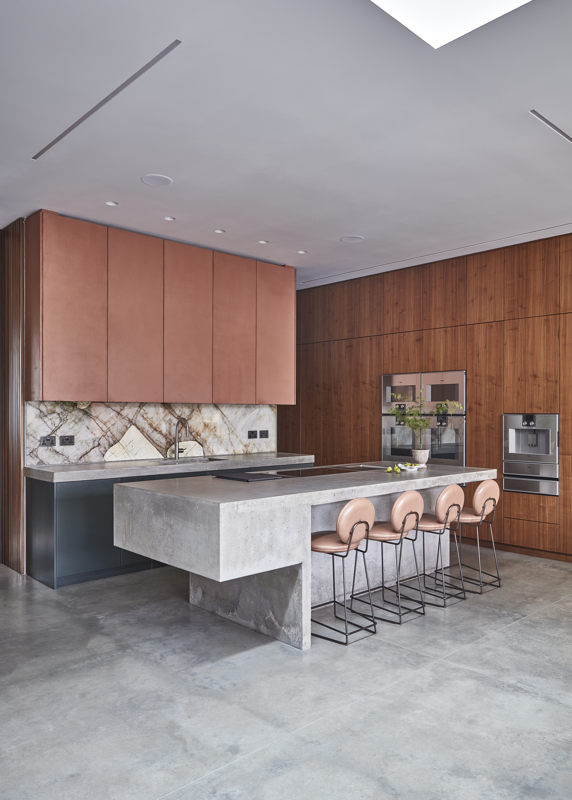 A kitchen with wooden vertical cabinets that stretch to the ceiling with a concrete style island and concrete style flooring