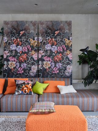 modern living room with gray and orange stripe sofa, cushions and foot stool, bold floral panel behind, plant, floral cushion, check cushion, tufted rug