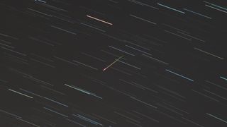 An Eta Aquarid meteor can be seen streaking from top right to bottom left against a backdrop of a night sky marked with multi-colored star trails.