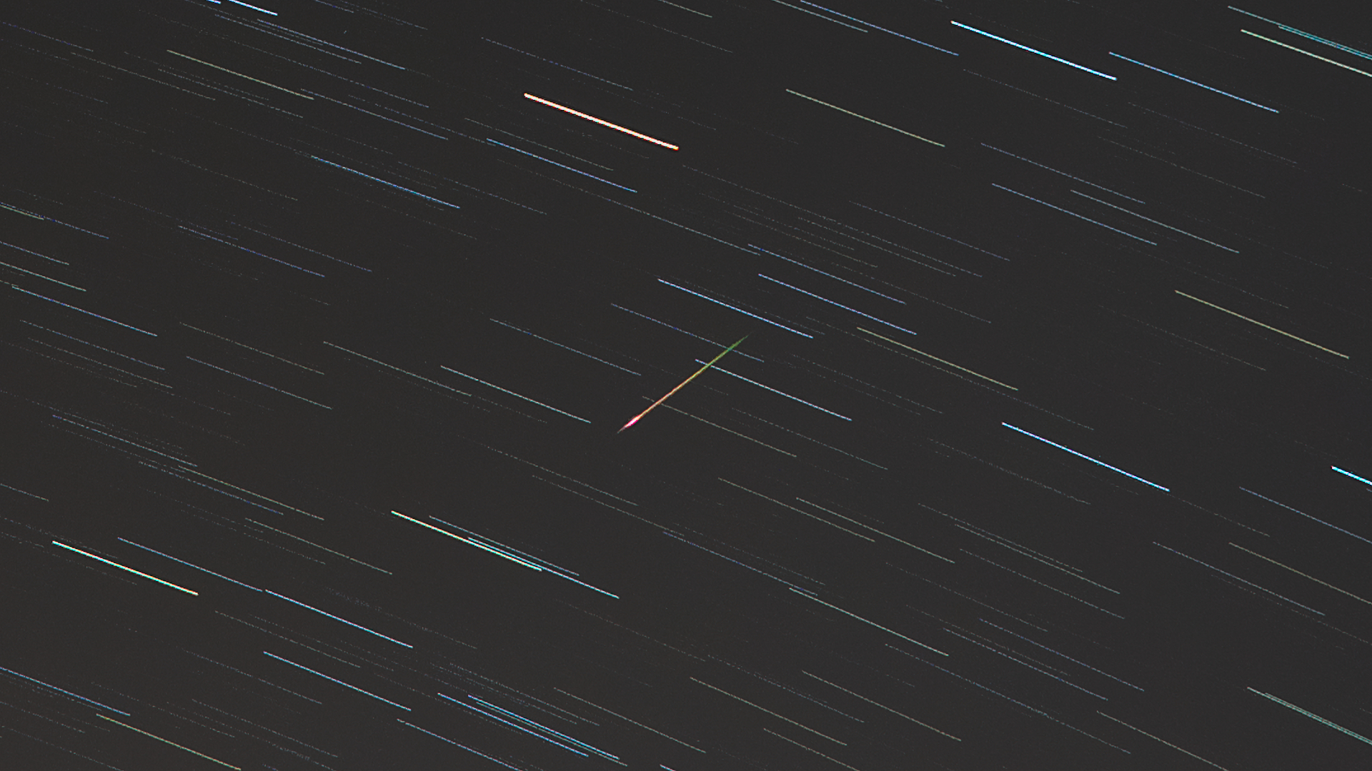 An Eta Aquarid meteor can be seen streaking from top right to bottom left against a backdrop of a night sky marked with multi-colored star trails. 