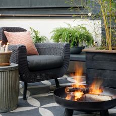 Black rattan chair next to black metal firepit in outdoor living space in garden