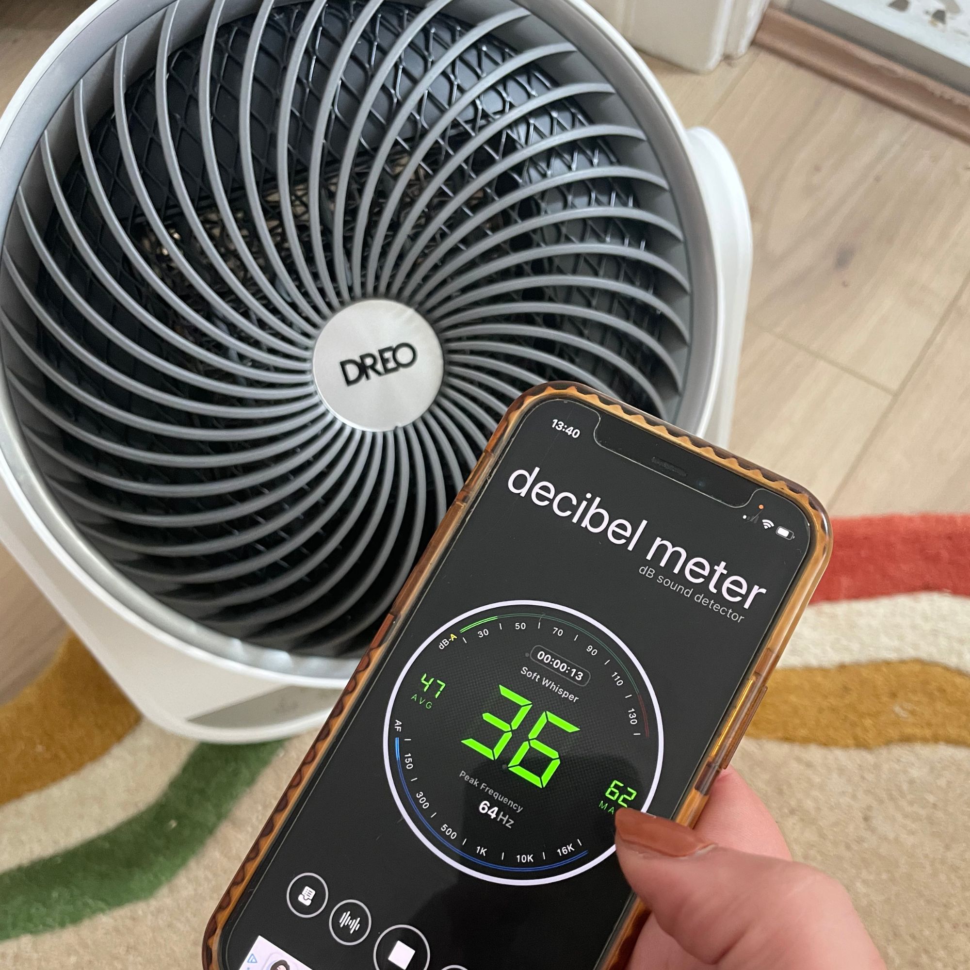 Dreo Smart Whole Room Heater 714S sitting on a rug, with a hand holding a phone in front of it