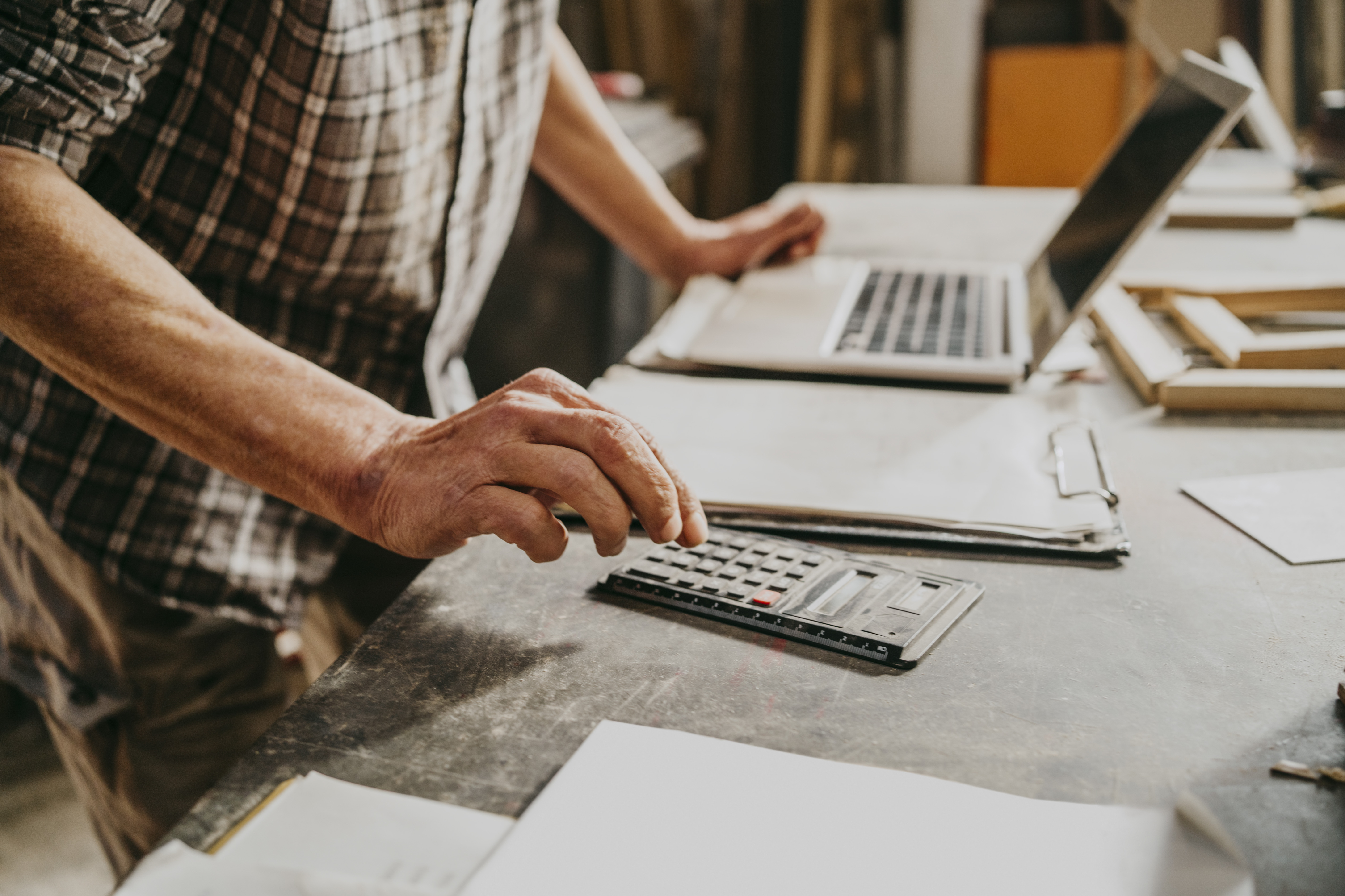 Person uses a calculator and a laptop while standing at a desk.