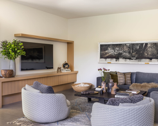 Living room with curved gray colored tub armchairs in front of wooden coffee table and couch rich with texture