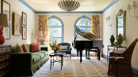 a light bright living room with neutral walls, blue painted trims, arched windows, grand piano and green skirted couch