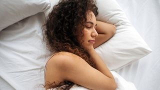 Woman with black curly hair sleeps on a white bed to get her beauty sleep at night