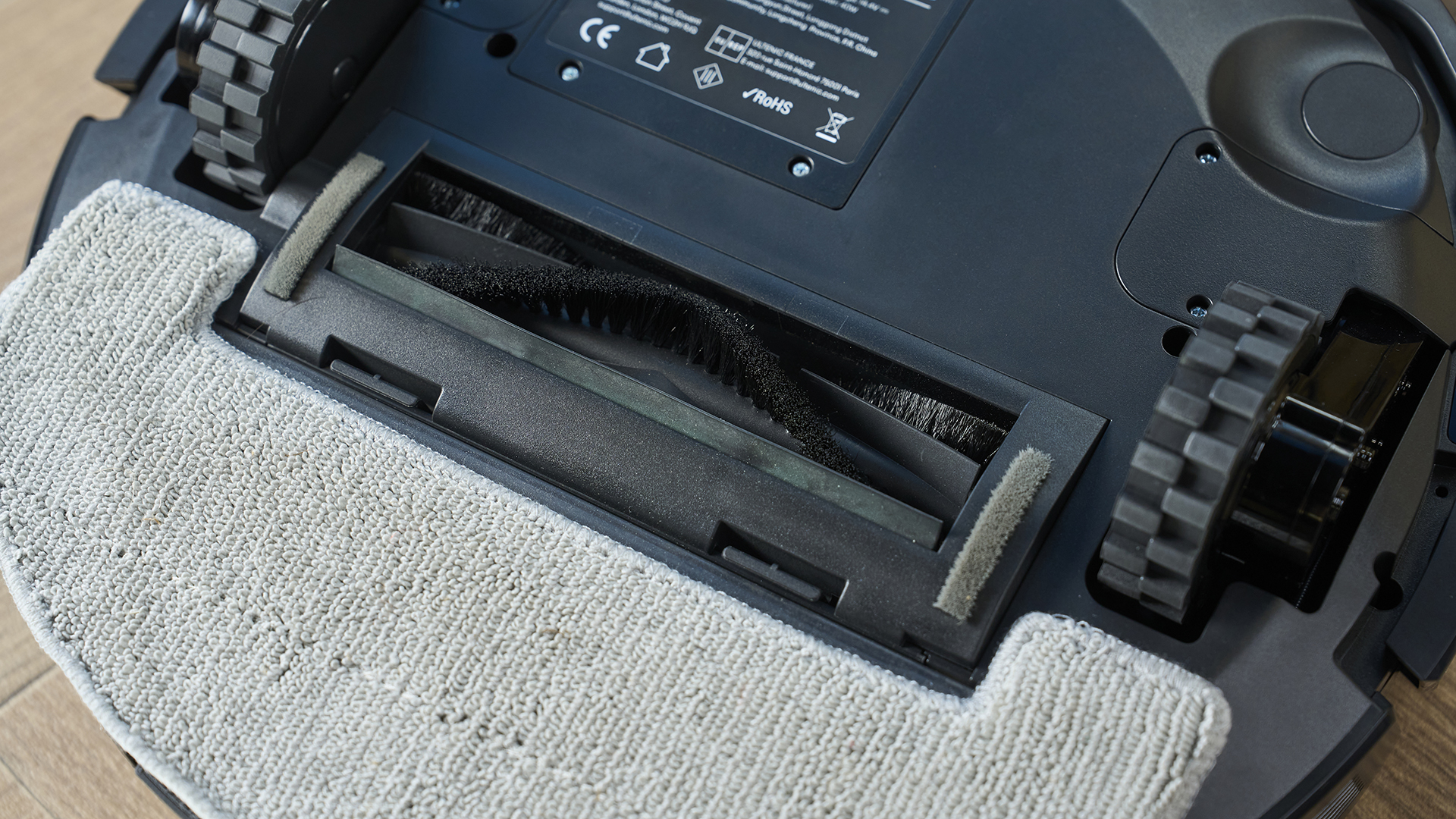 a rechargeable robot vacuum and mop in black by ultenic is photographed on a hardwood floor with a blue wall and a burnt orange terracotta and white striped rug