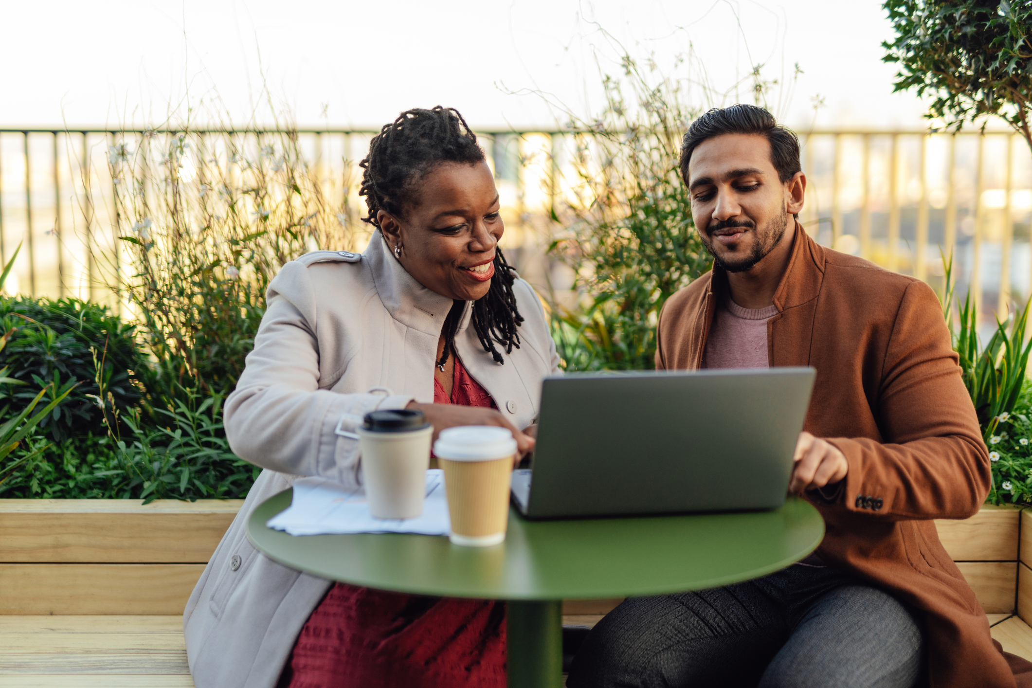 Two people discussing their investments over a laptop, working outside, surrounded by greenery