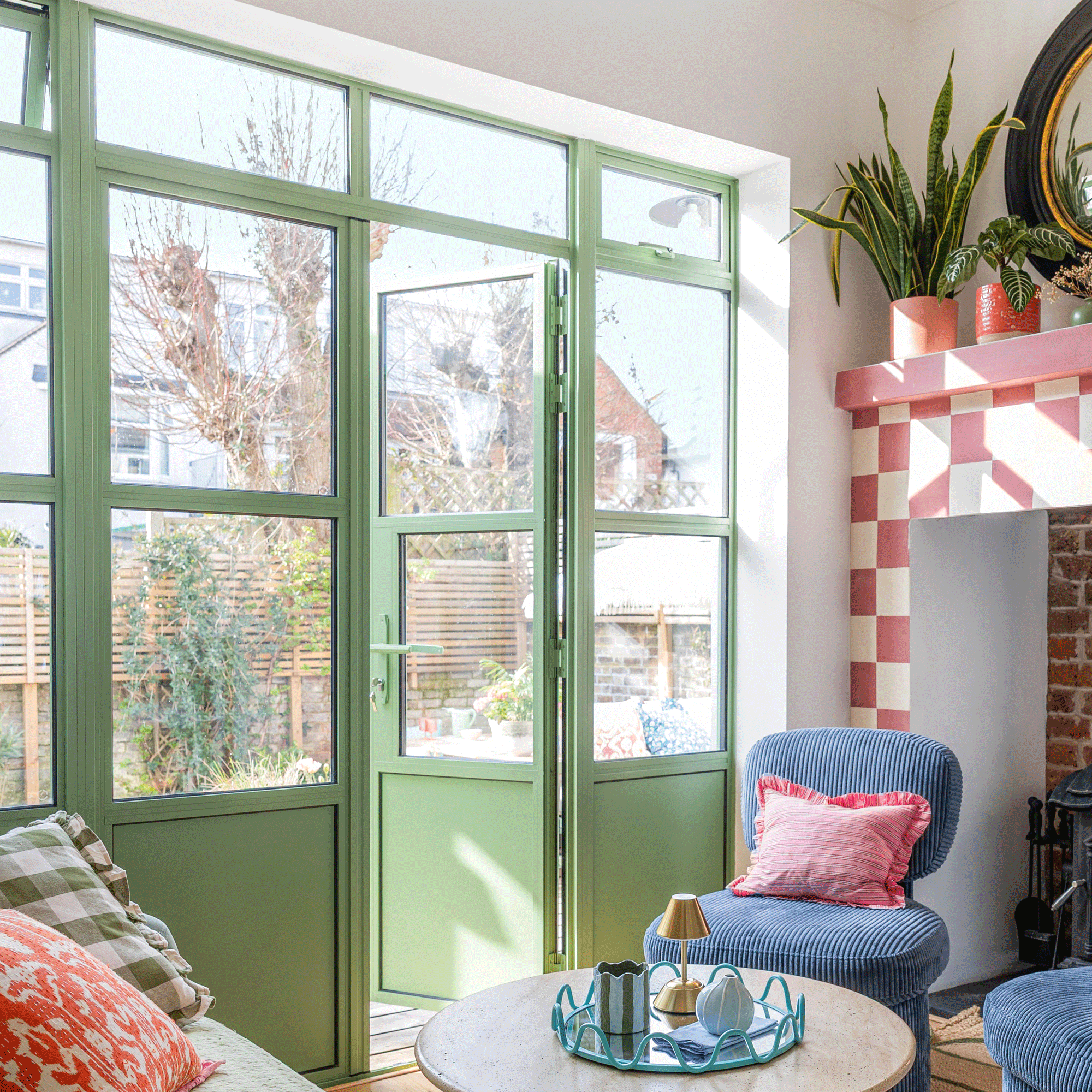 a set of green patio doors beside a checkered painted fire surround leading into a decked garden