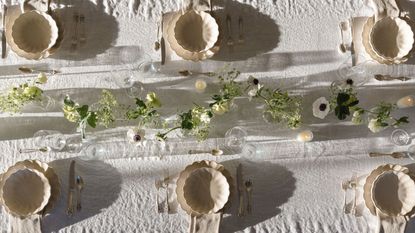 Outdoor tablescape with white linen tablescape, cream scalloped plates and bowls, a floral garland in the centre, and lit candles