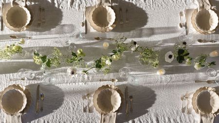 Outdoor tablescape with white linen tablescape, cream scalloped plates and bowls, a floral garland in the centre, and lit candles
