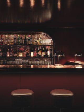 A cherryplum-drenched bar boasts marble countertops, sleek table lights, and an Art Deco-inspired atmosphere.