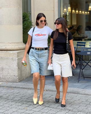 Two women walking toward the camera wearing long denim shorts and t-shirts.