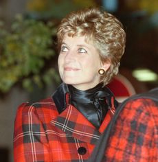 Princess Diana in a red plaid blazer and black scarf looking up and smiling