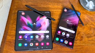 galaxy s22 ultra and galaxy z fold 3 laying side by side on table with s pens out