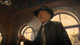 Indiana Jones grimaces as he cracks his iconic whip at some bad guys off screen in his Dial of Destiny movie