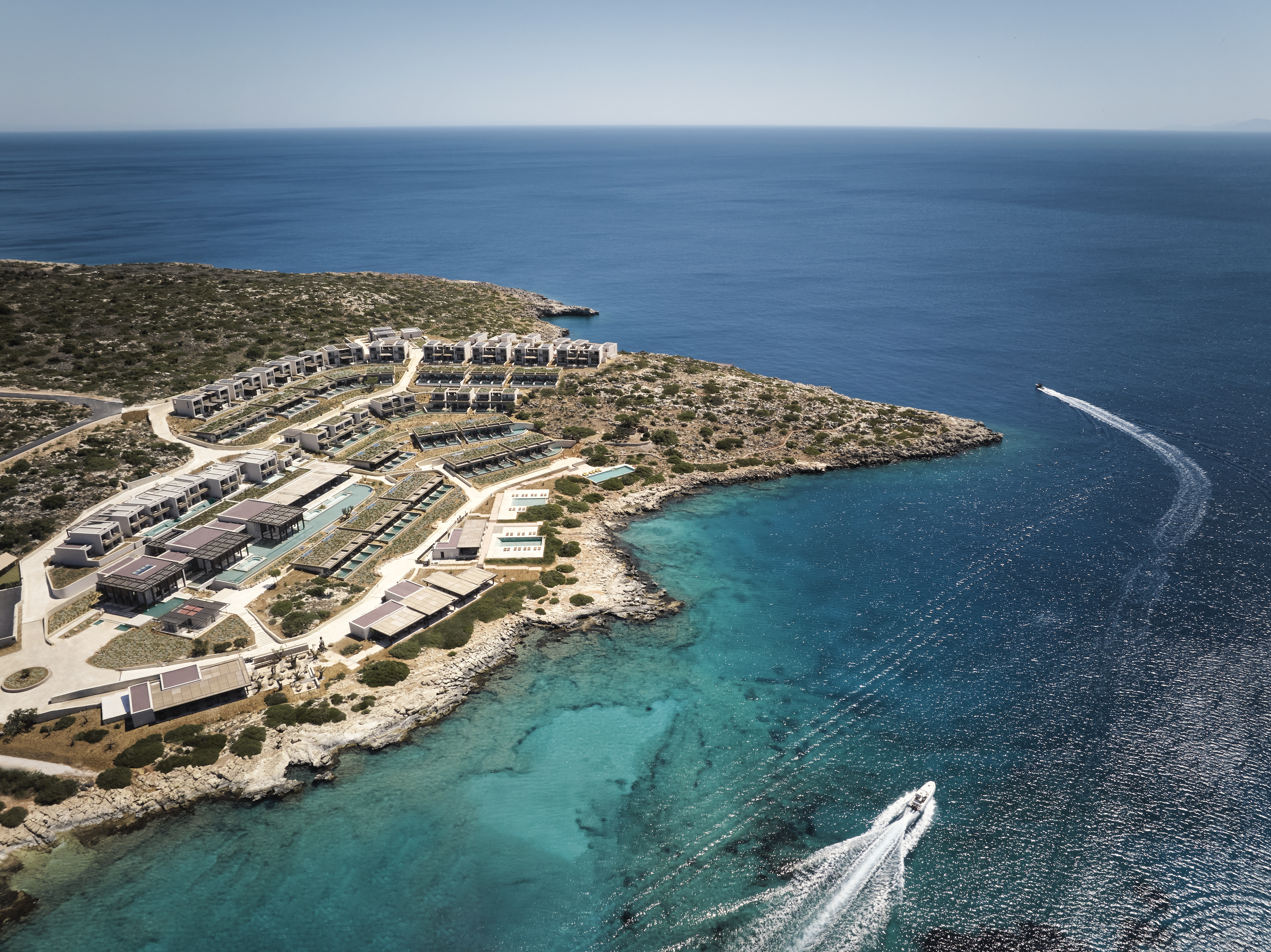 areal view of the JW Marriott Crete on a sunny day showing a turquoise blue sea and a speed boat.