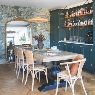 dining room with large mirror, botanical wallpaper and built in blue panelled bar area and wooden table and chairs