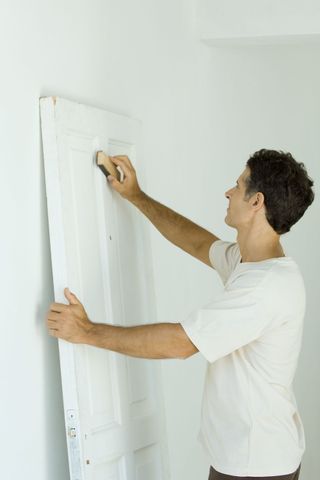 A man sanding a white painted door