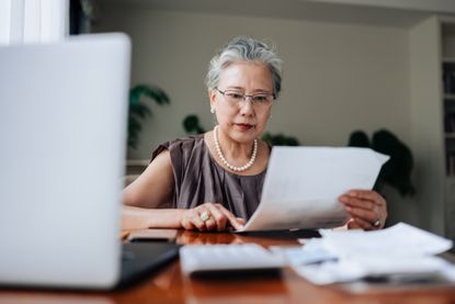 A senior woman reviews financial paperwork at her desk.