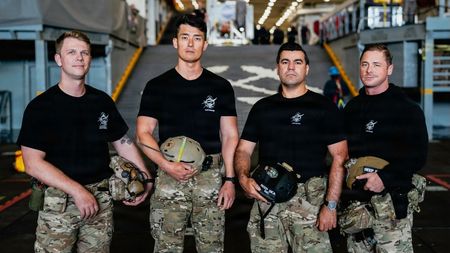 Steve Kapala, Jesse Wang, Vlad Link and Laddy Aldridge of the U.S. Navy dive medical team pose aboard the USS John P. Murtha ahead of Artemis 2 recovery operations in the Pacific Ocean.