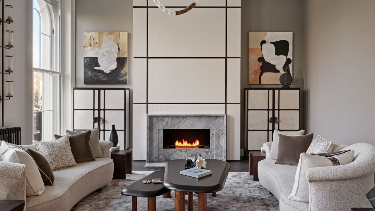 living room with pale walls and fire lit white sofas and modern artworks in alcoves and parquet floor