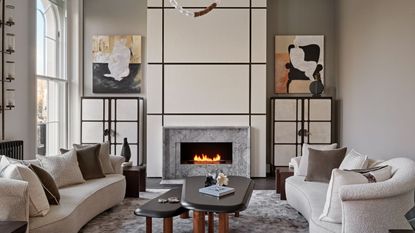 living room with pale walls and fire lit white sofas and modern artworks in alcoves and parquet floor