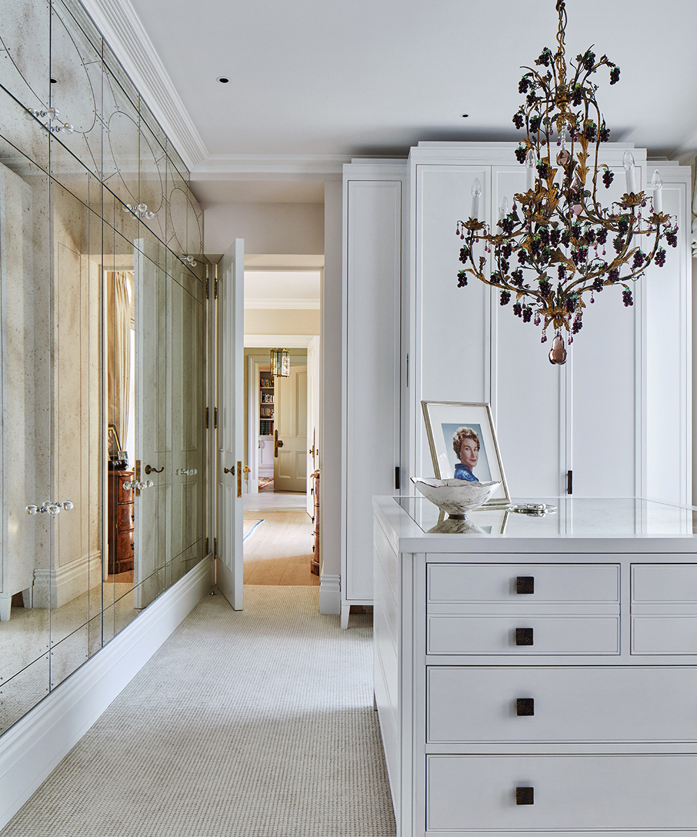 A white walk-in closet with mirrored doors and a large, gold chandelier